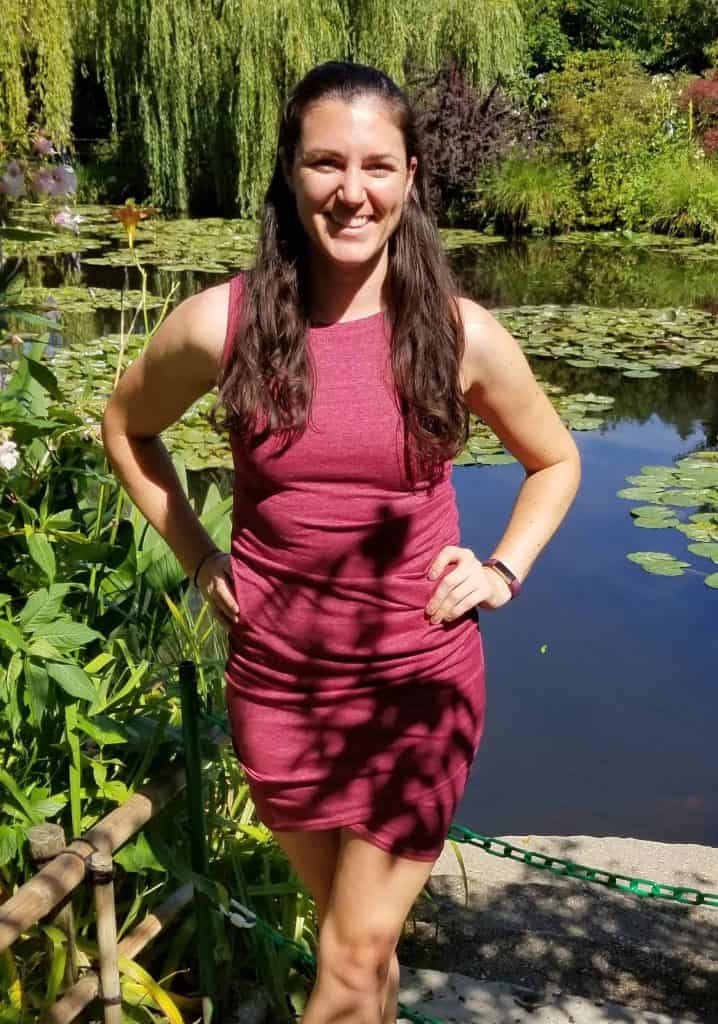 Michele (PT) stands smiling in front of a pond with water lilies