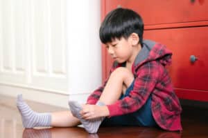 Example of an ADL Child sitting on floor putting on a grey sock; dressing is an ADL - functional skills in pediatric