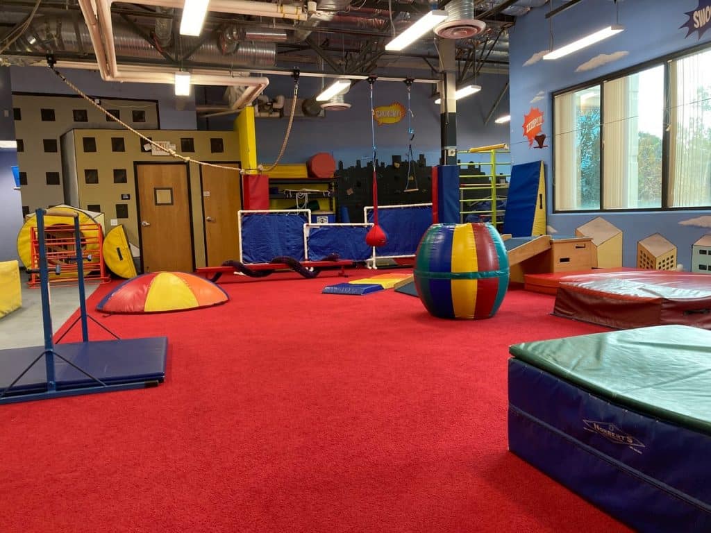 My Kids Place's colorful gym with balance beam, tunnel, parallel bar, and red carpeted floor