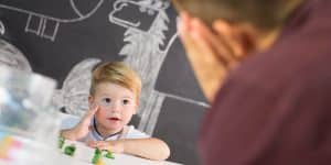 Child looking at teacher with small toys on table between them | social skills and overall child development