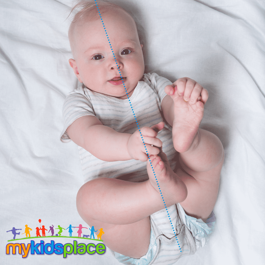 A baby in a white/grey striped onesie is lying on their back reaching for their feet at midline with both hands. Midline is represented by a blue dotted line reaching from head to bottom in the middle of the eyes, nose, chin, and body.
