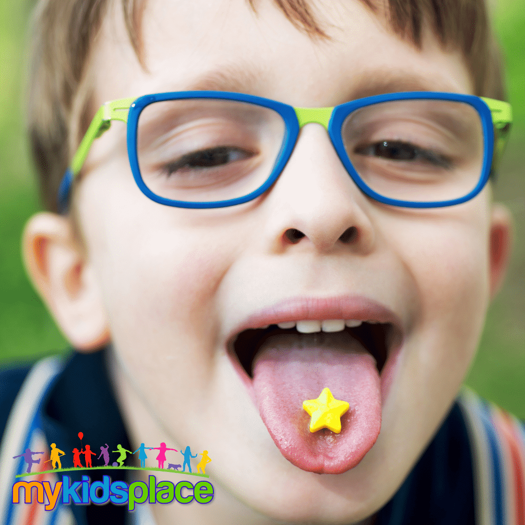 Child with blue glasses sticks their tongue out which is holding a yellow star-shaped candy to depict the sense of taste (gustatory).