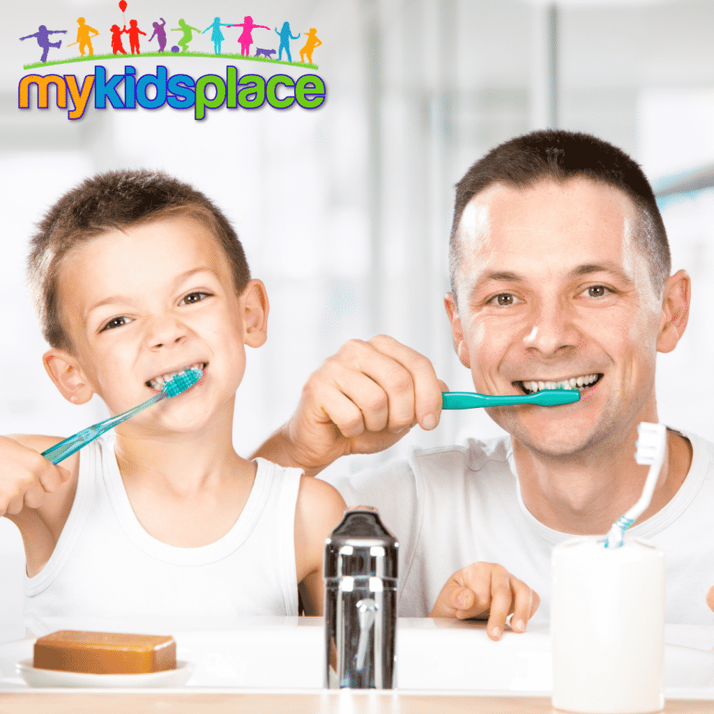 A parent and child in white shirts facing the camera brush their teeth; an essential activity of daily living.