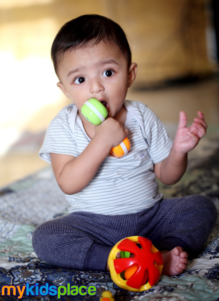 Baby sitting on the floor places a toy in their mouth as a demonstration of sensory play