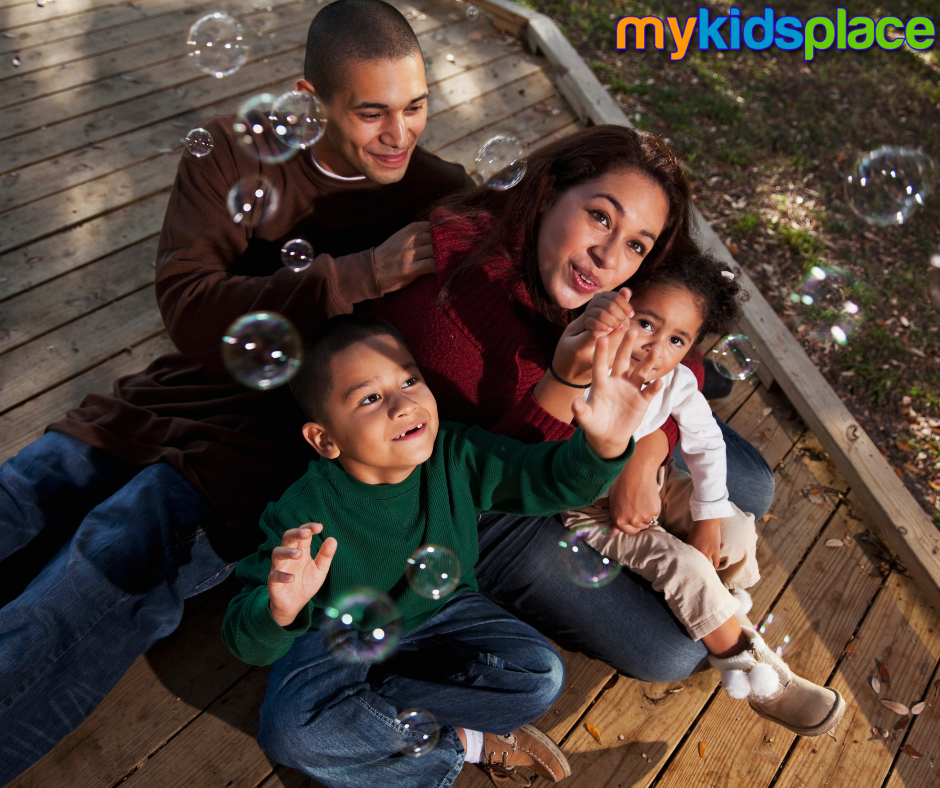 A happy family of 4 plays outside together by blowing bubbles | play child development