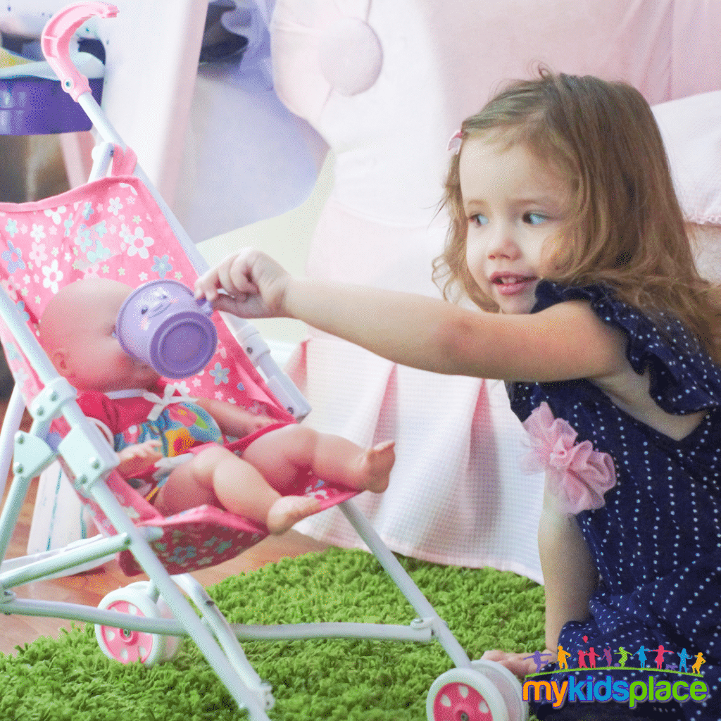 A child pretends to feed a doll sitting in a stroller