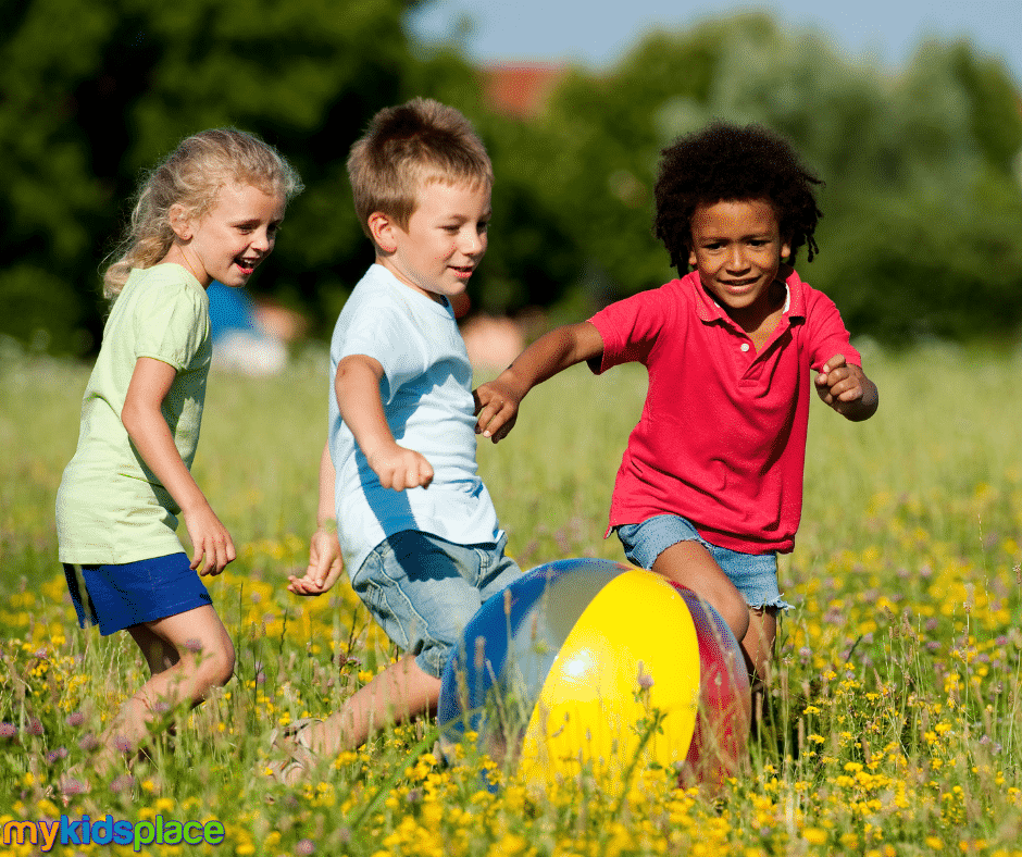 Three children chase a beach ball in a flower field