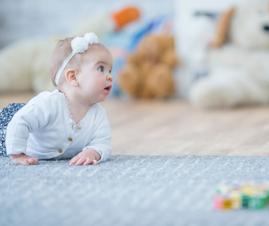 A baby mid-crawl on the carpet looks up to see where they want to go.