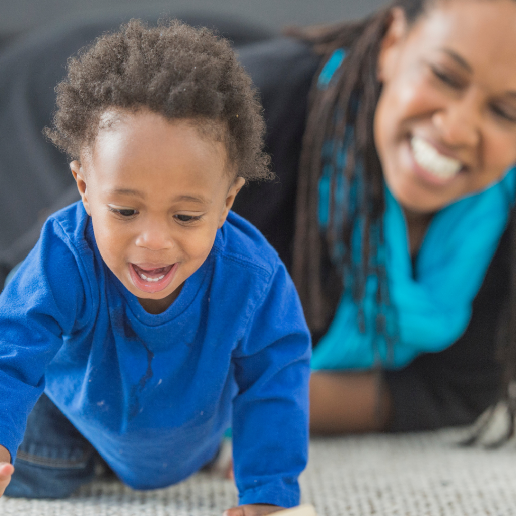 A child creeps toward the camera as the mother is in the background smiling as she watches her child.