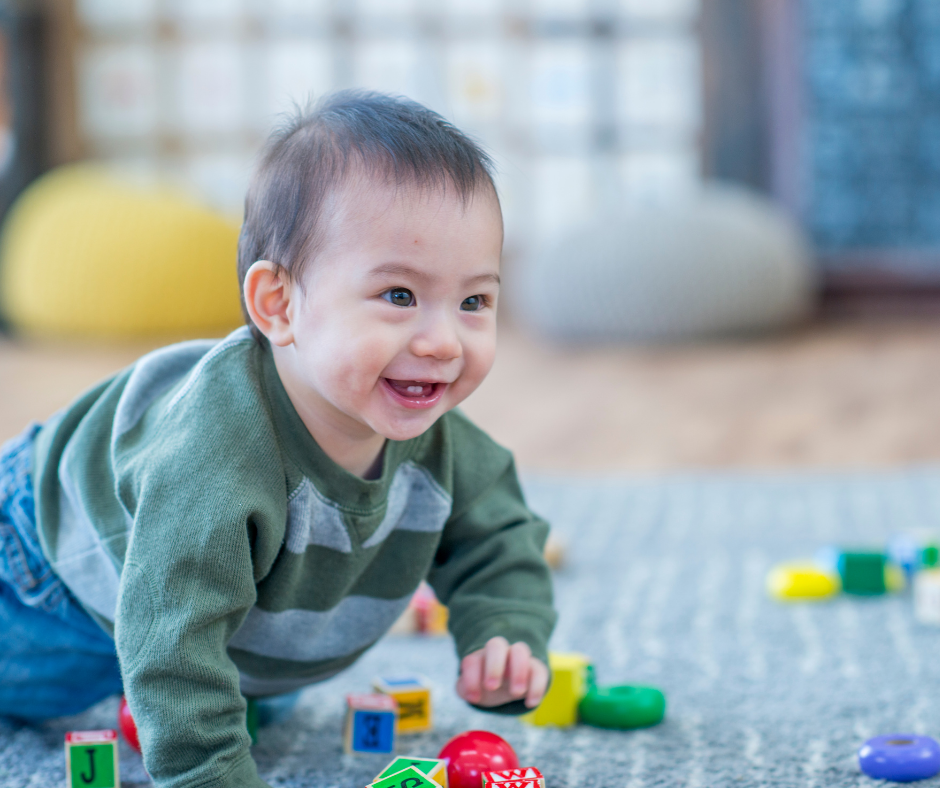 A smiling baby creeps around colorful toys.