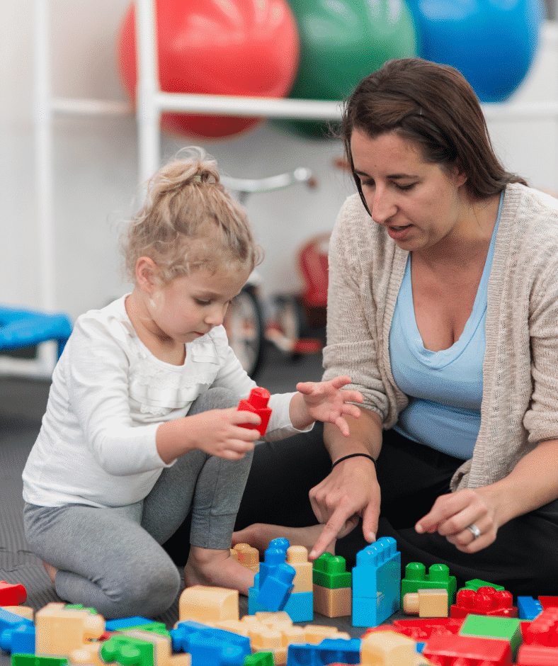 An occupational therapist points to a yellow block where a child can place the red building block they have.