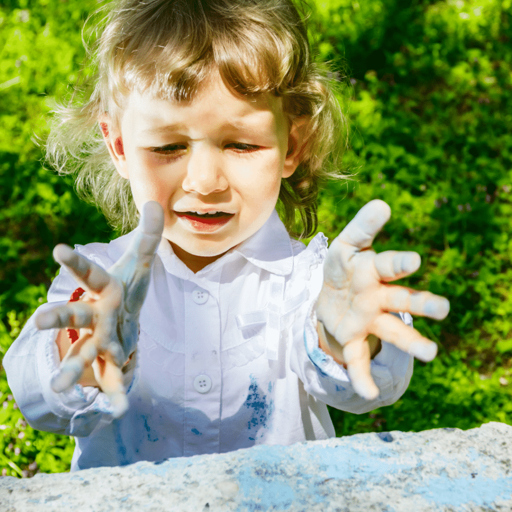 A child with a worried expression looks at their hands covered in blue chalk.