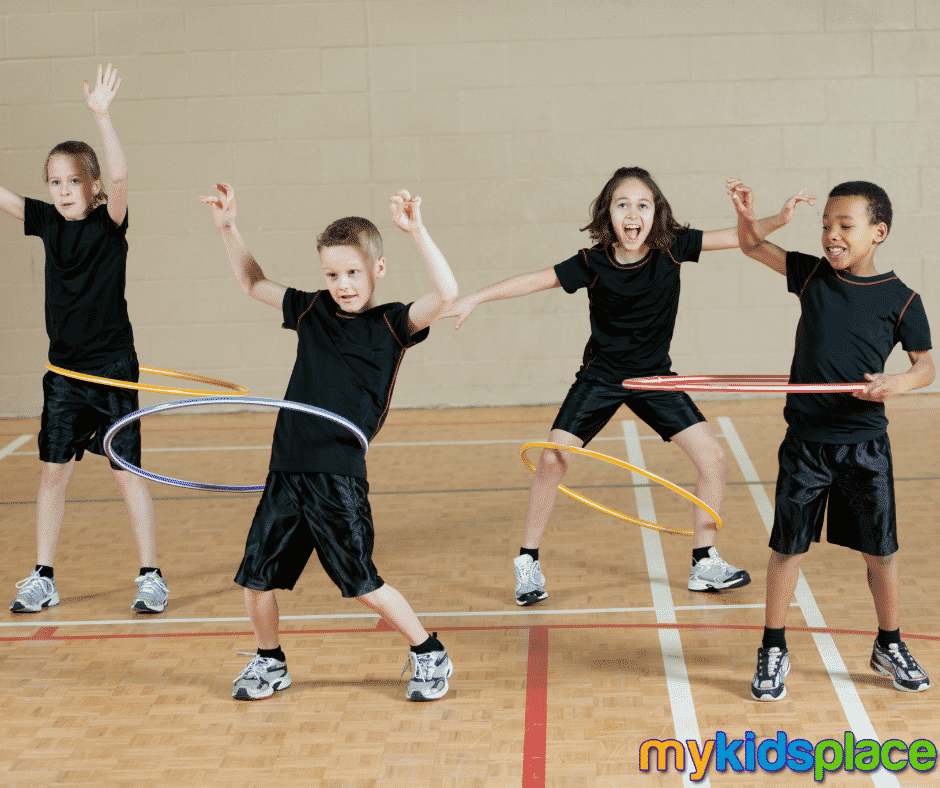 Four children wearing black shorts and shirts practice hula hooping and try to avoid bumping into each other as a way to improve spatial awareness.