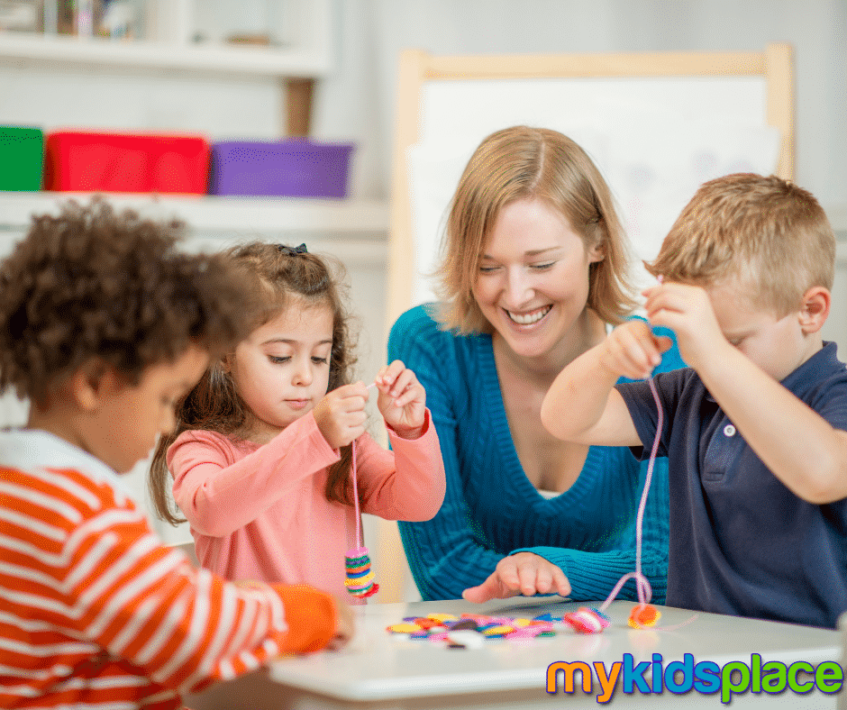 Three young children and a teacher practice stringing colorful buttons on strings to improve their fine motor control.
